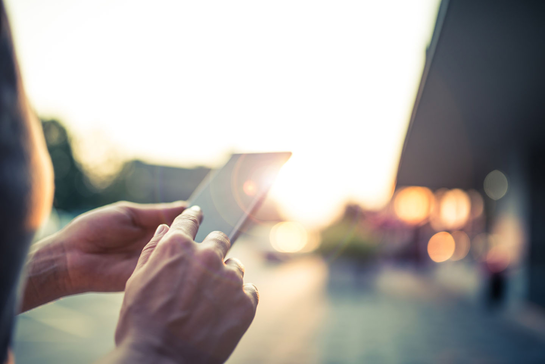 Woman using her Mobile Phone sending messages or taking pictures in the street. Magic lights at sun set